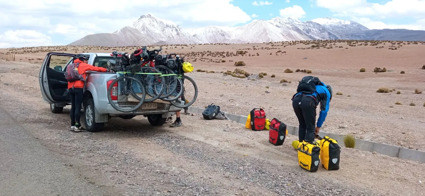 Bicicletas de bikepacking cargadas en la parrilla de la camioneta, alforjas junto al camino, volcanes nevados de fondo