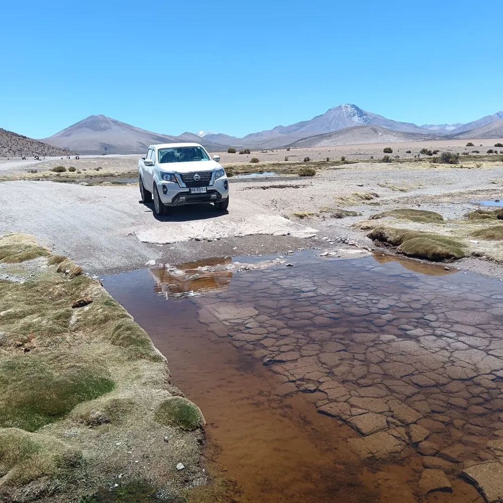 Camioneta 4x4 cruzando un bofedal con volcanes de fondo, ruta altiplánica Arica-Iquique