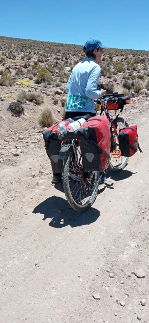 Ciclista bikepacker alejándose con su bicicleta cargada con alforjas rojas por un camino de tierra