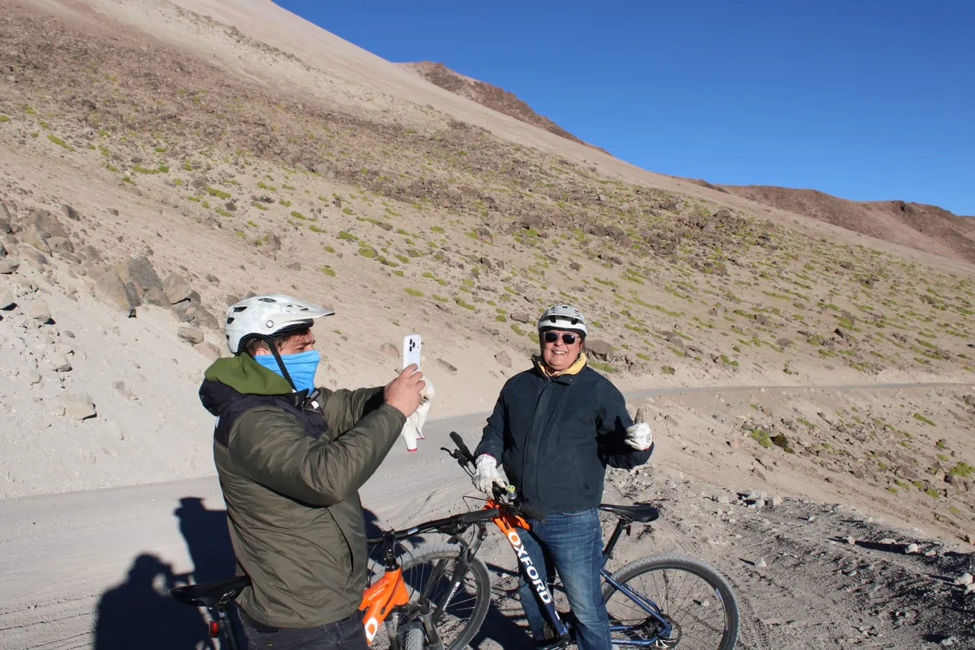 Ciclista fotografiando con su celular a su compañero, que hace un gesto de pulgar arriba