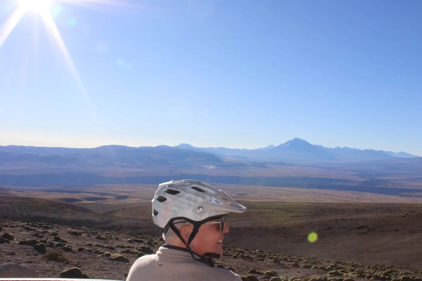 Ciclista de perfil observando un volcán en el horizonte, vegetación de altiplano en primer plano