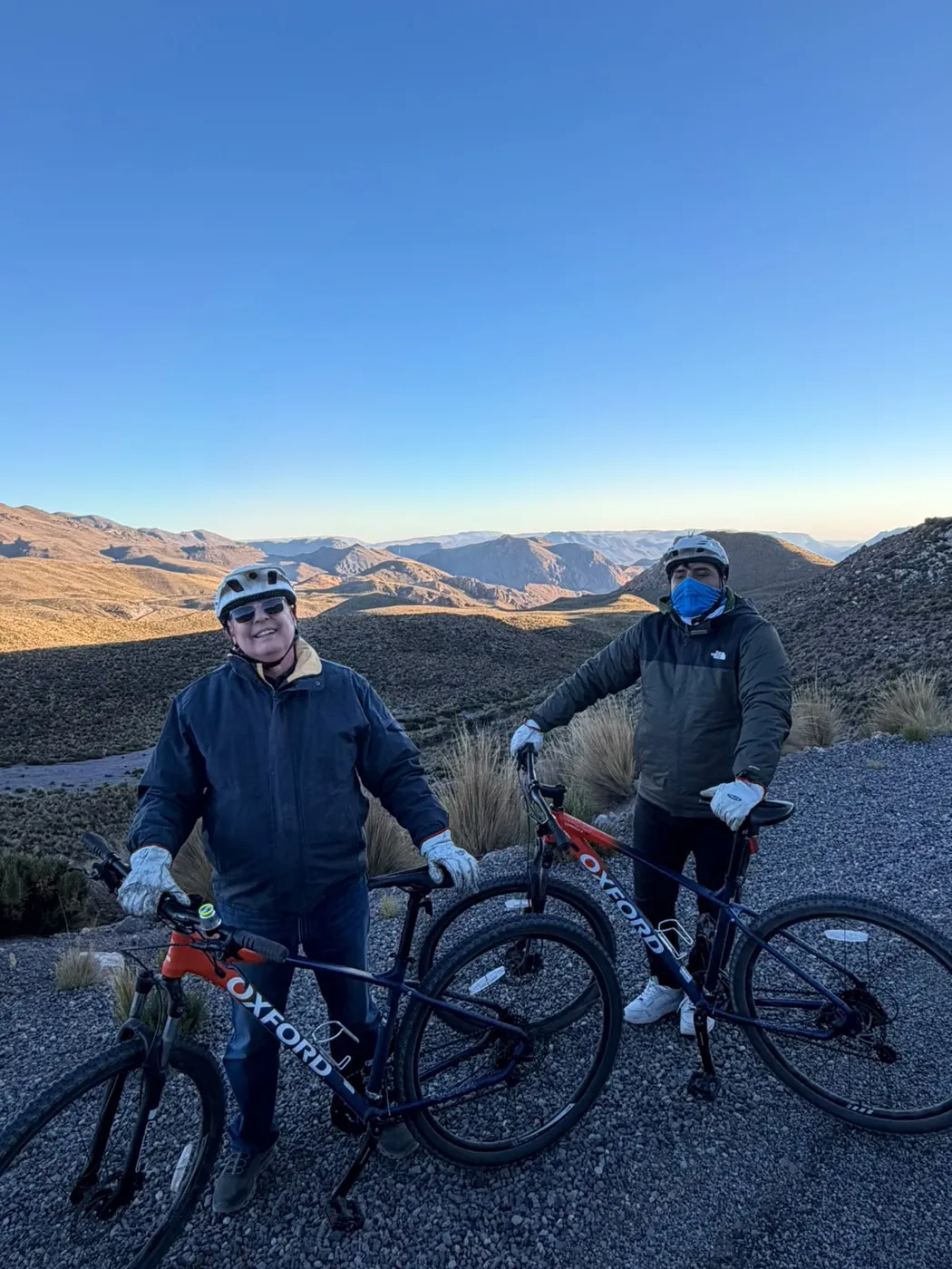 Dos ciclistas posando con sus bicicletas al atardecer, cerros del altiplano de fondo