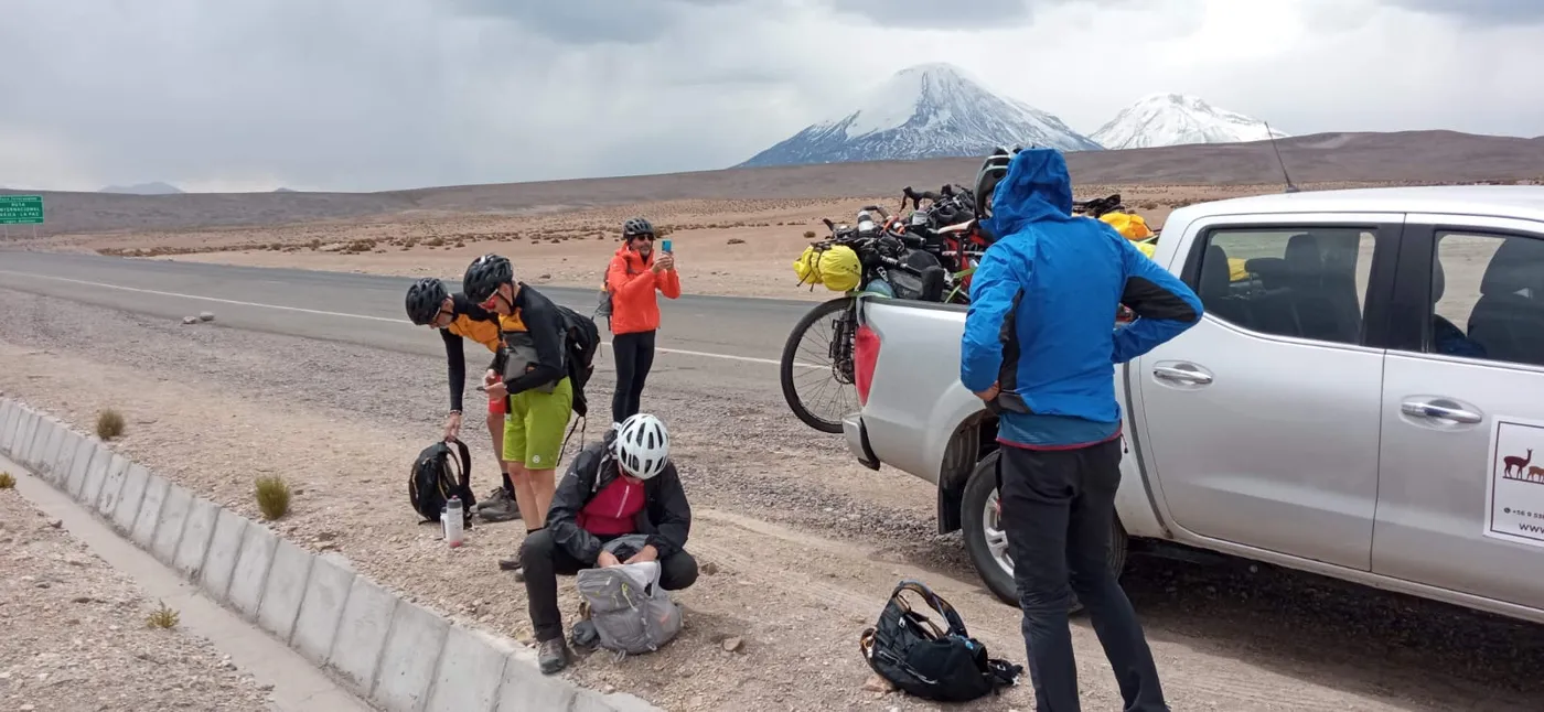 Grupo de ciclistas bikepackers alistándose junto a la carretera con los volcanes del altiplano de fondo