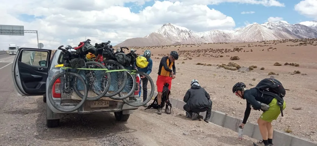 Grupo de ciclistas bikepackers preparando el equipaje junto a la carretera, cordillera nevada al fondo