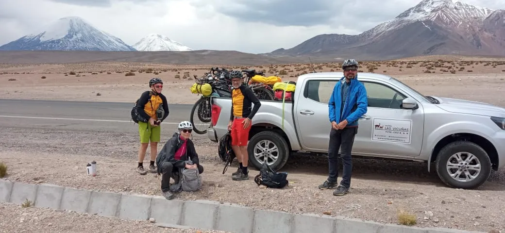 Grupo de ciclistas bikepackers posando junto a la camioneta con los volcanes nevados de fondo