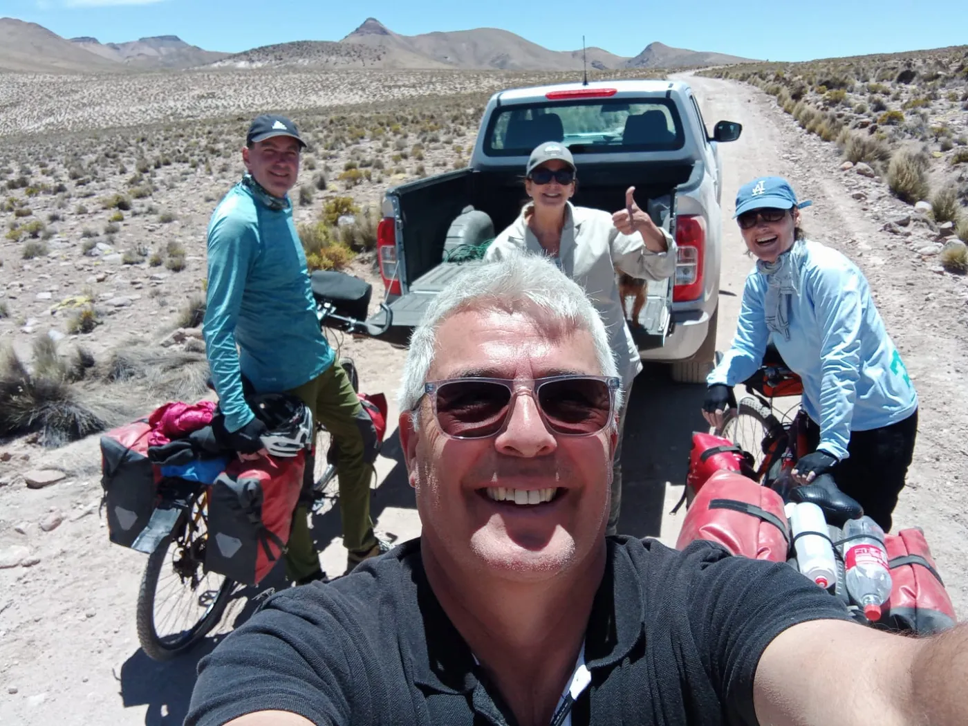 Selfie grupal de ciclistas bikepackers con sus bicicletas cargadas, camioneta de apoyo al fondo
