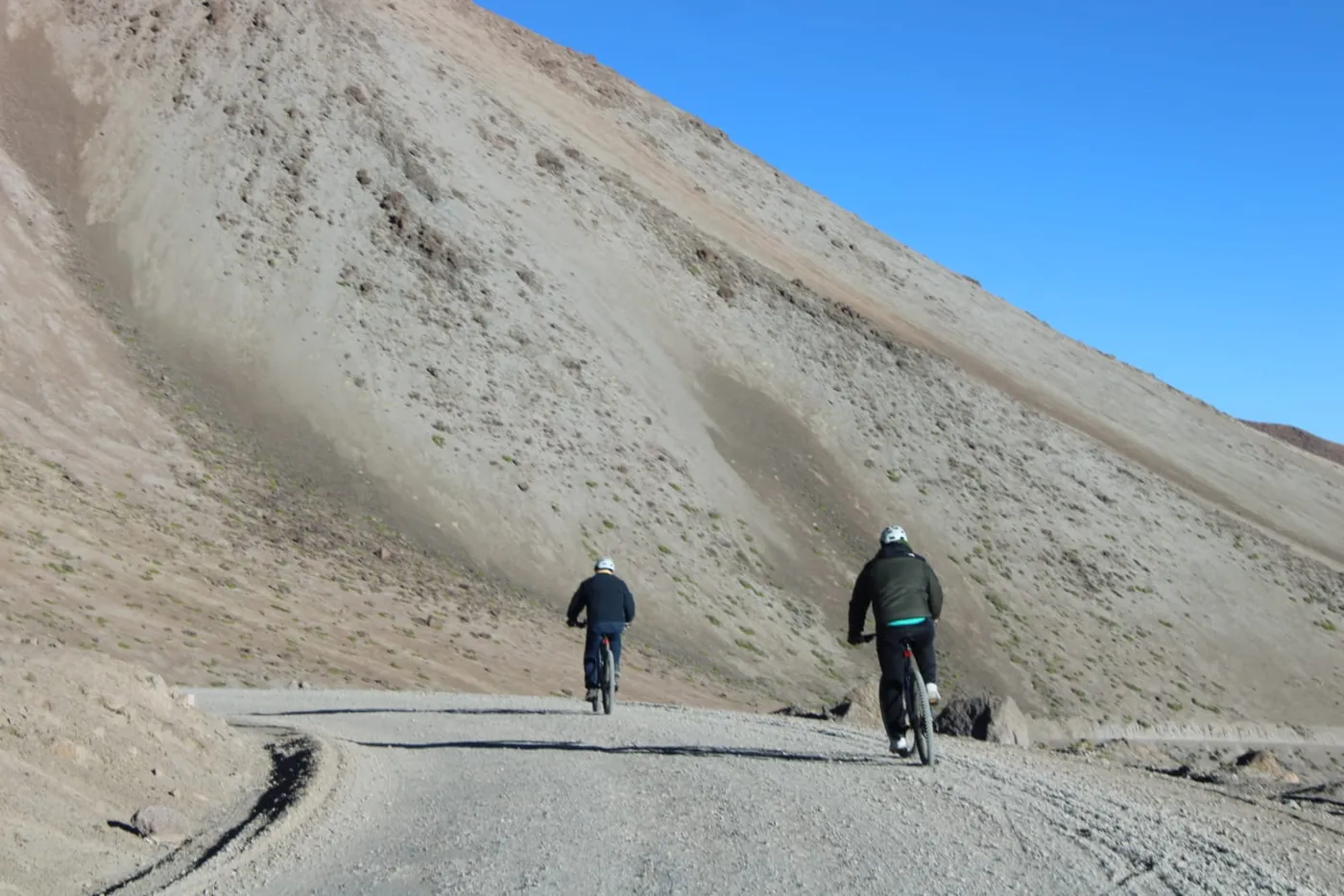 Dos ciclistas descendiendo por camino de tierra al pie de una ladera árida