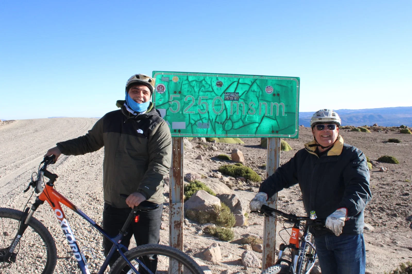 Dos ciclistas con sus bicicletas en el cartel de los 5.250 m.s.n.m.