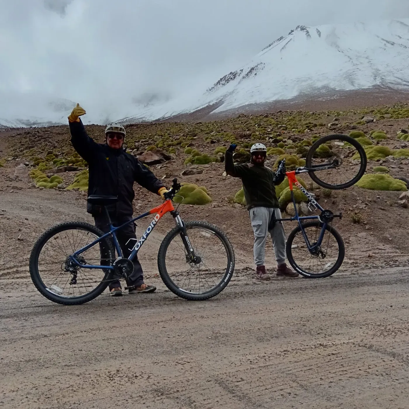 Ciclistas celebrando con las bicicletas en alto frente al volcán nevado