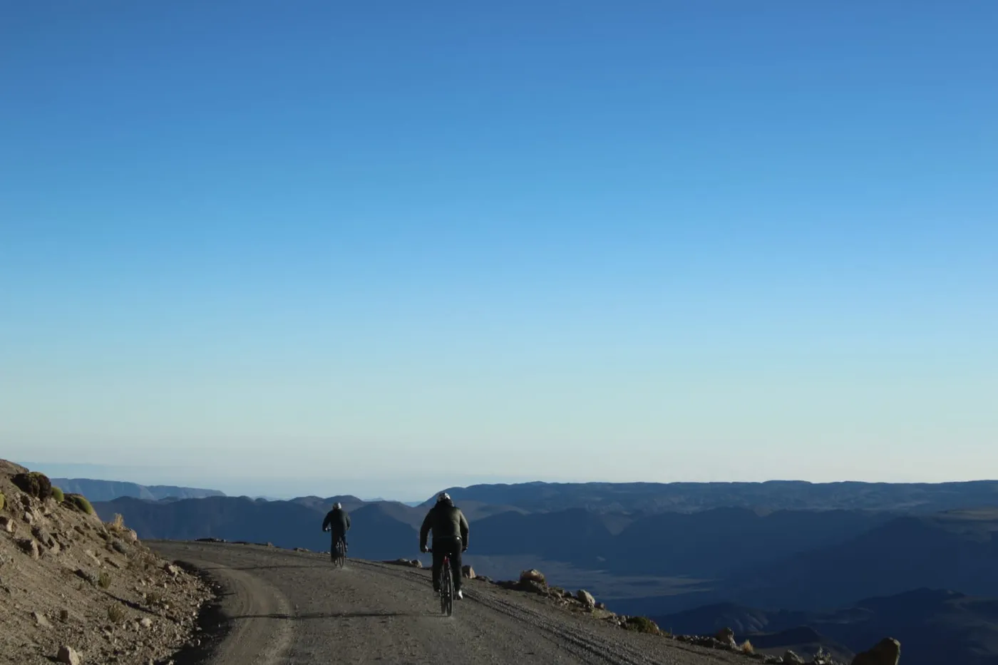 Dos ciclistas pedaleando hacia el cielo despejado sobre la cresta del camino