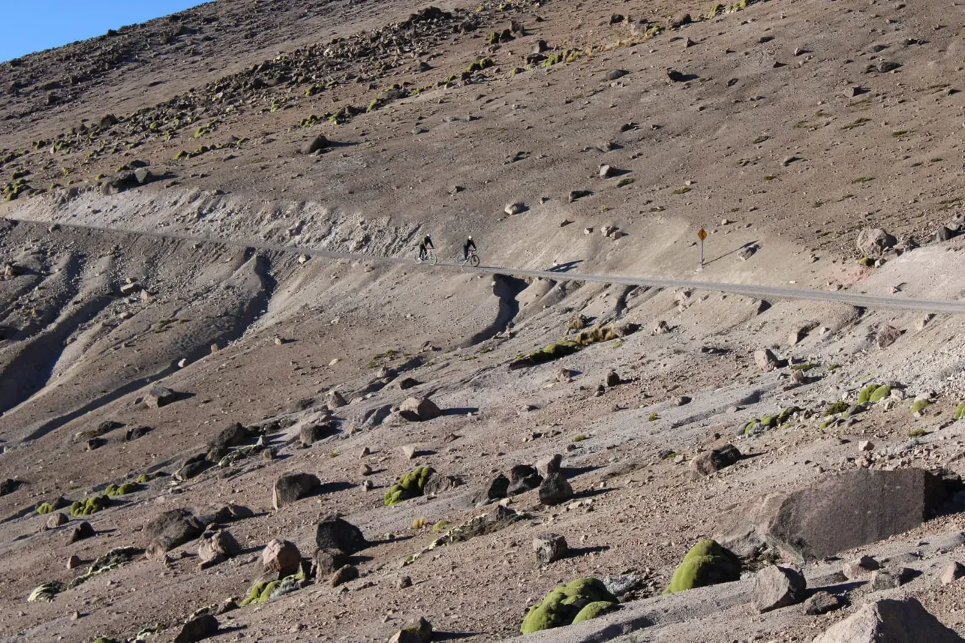 Vista lejana de dos ciclistas sobre un camino que cruza una ladera del altiplano