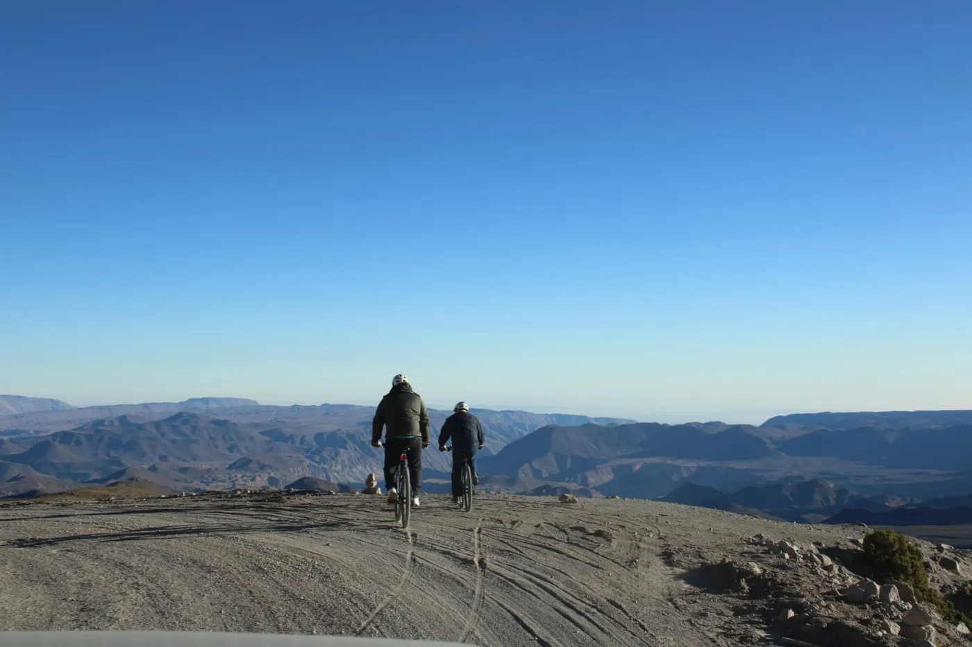 Dos ciclistas alejándose por camino de tierra sobre una meseta, cordillera de fondo