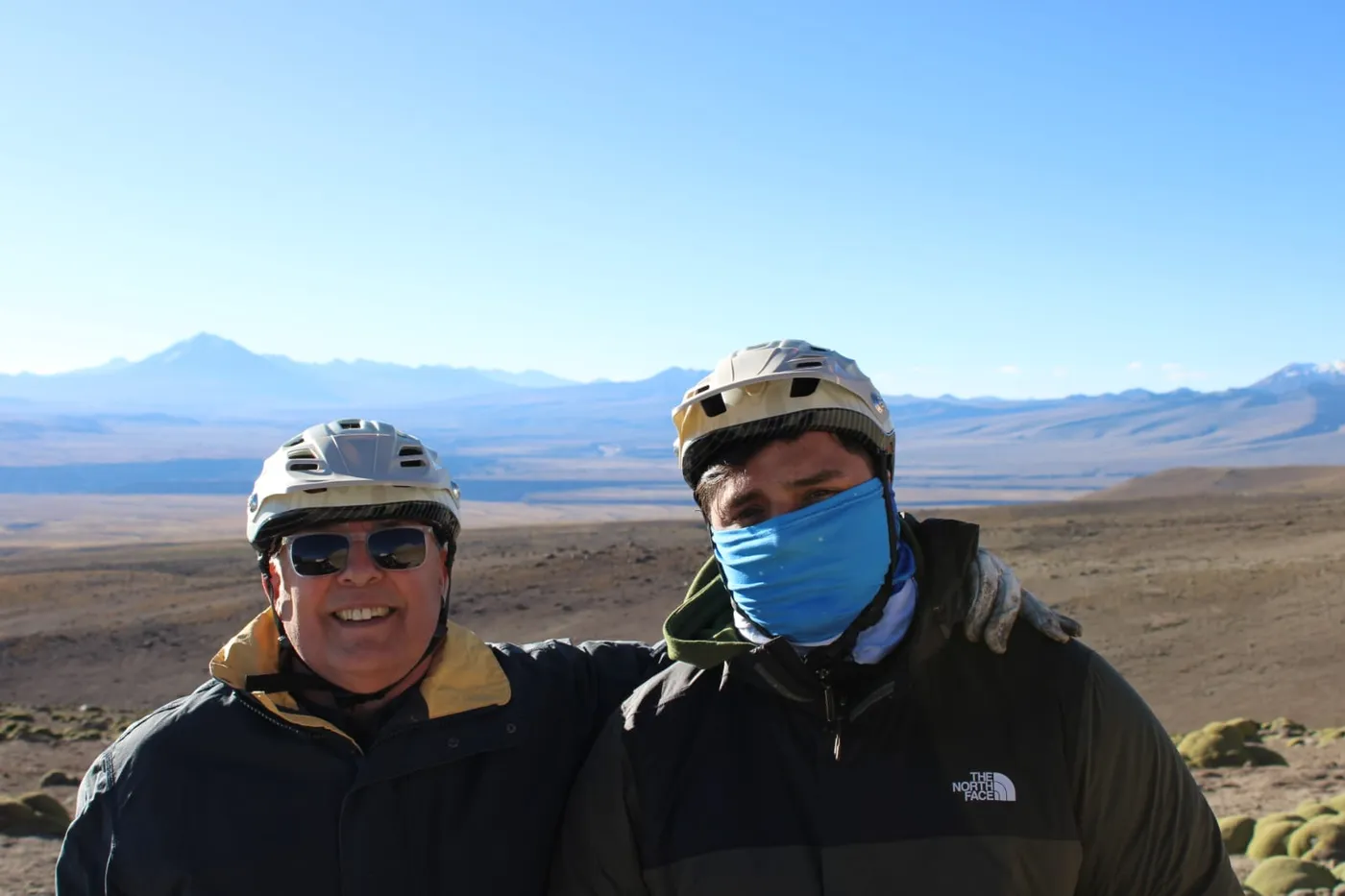 Retrato de dos ciclistas sonriendo con volcanes nevados de fondo