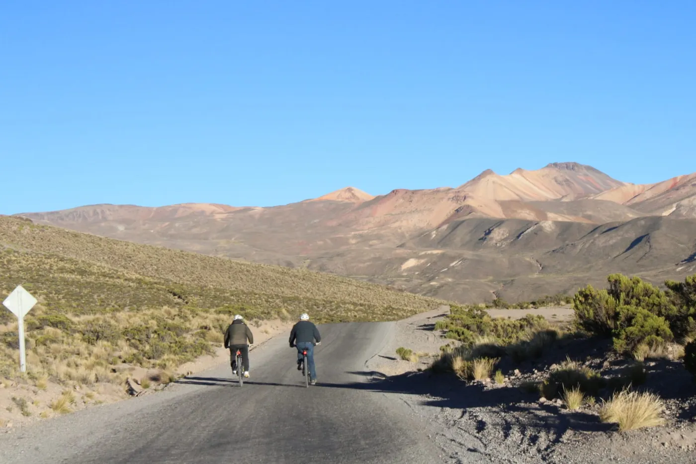 Dos ciclistas pedaleando con montañas de tonos rojizos y ocres de fondo