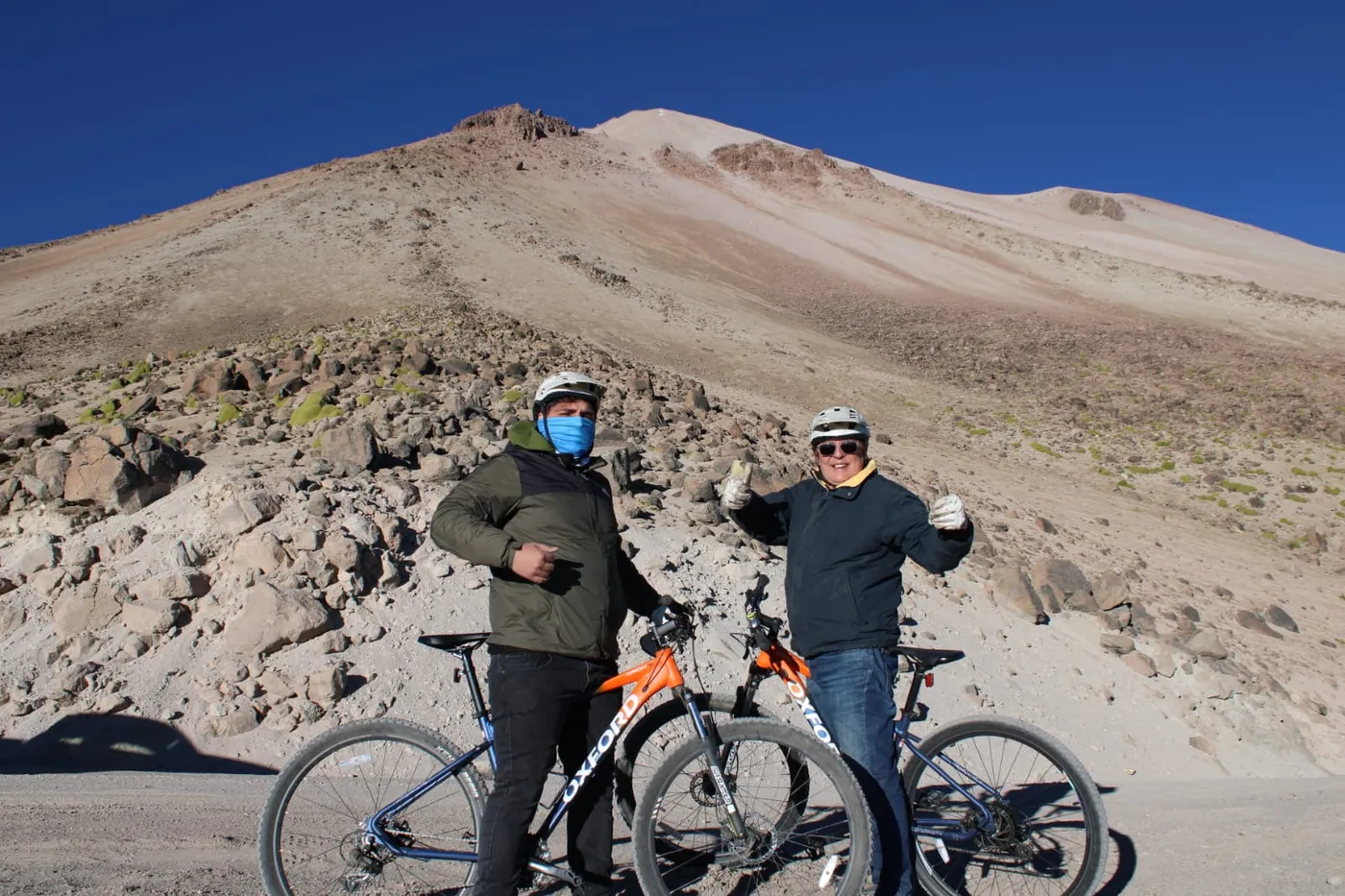 Ciclistas celebrando frente al volcán, pulgares arriba